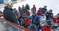 Hockey coach talking to a group of young players on the ice, as they gather closely around him.